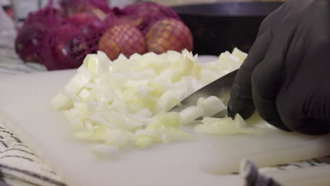 White-onion-sliced,-diced-with-knife-on-cutting-board-by-gloved-hands