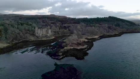 Dunvegan-castle-on-the-isle-of-skye,-surrounded-by-woodland-and-coastline-at-dusk,-aerial-view