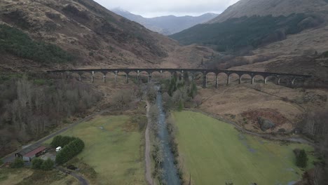 The-historic-glenfinnan-viaduct-in-scotland,-surrounded-by-rugged-landscapes-and-greenery,-aerial-view
