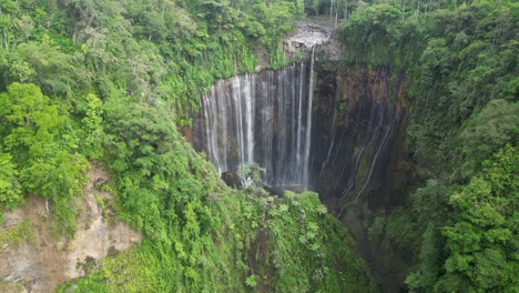 Surreal-waterfall-Tumpak-Sewu-falls-into-deep-jungle-grotto,-Java-IDN