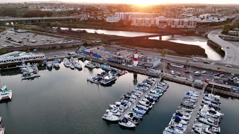Oceanside-harbor-with-boats-docked-at-sunrise,-calm-waters-reflecting-light,-aerial-view
