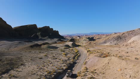 Following-a-white-vehicle-driving-through-desert-hills,-Utah,-Western-USA