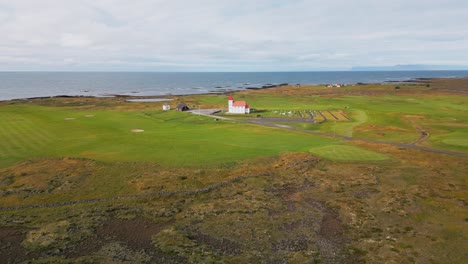 Parallax-view,-quiet-icelandic-village-with-golf-field,-red-roof-church-and-green-nature