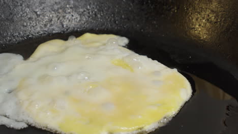 Pan-across-egg-frying-in-butter-in-hot-cast-iron-skillet,-close-up