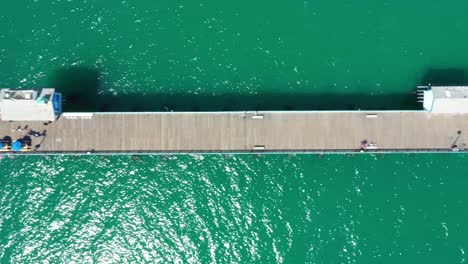 Aerial-top-down-4k-view-over-San-Clemente-Pier,-from-end-to-end,-with-emerald-water-and-people-walking-on-pier
