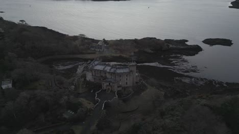 Dunvegan-castle-on-isle-of-skye,-surrounded-by-trees-and-water-at-dusk,-aerial-view