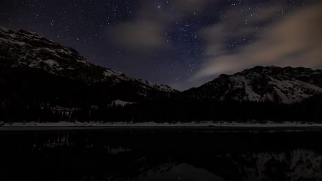 Night-sky-time-lapse-with-snowy-mountains-reflected-in-alpine-lake,-Italy