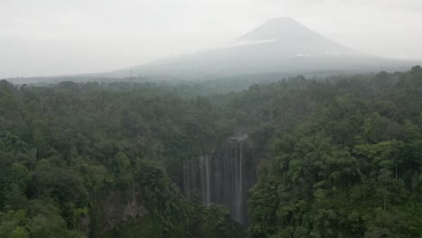 Aerial-rotates-over-misty,-hazy-Tumpak-Sewu-waterfall-and-Java-volcano
