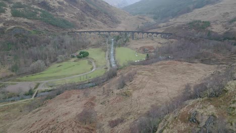 The-historic-glenfinnan-viaduct-in-scotland,-surrounded-by-scenic-landscapes-and-verdant-hills,-aerial-view