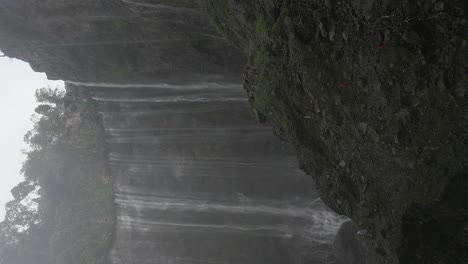 Misty-humid-vertical-aerial-retreats-from-Tumpak-Sewu-waterfall,-Java