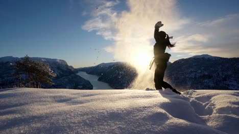 Young-woman-throws-snow-up-in-the-air-in-front-of-sunset,-Hiking-Norway-fjords