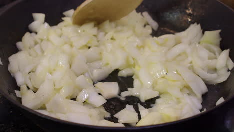 Close-up:-Wooden-spoon-stirs-diced-onions-frying-in-hot-cast-iron-pan
