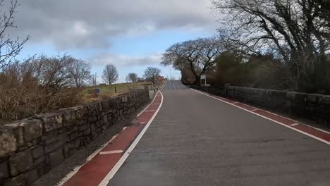 Rural-road-in-Scotland-with-stone-walls,-leafless-trees,-and-overcast-skies,-car-POV