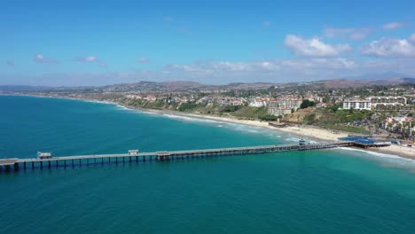 Aerial-4k-Slider-shot-45-degree-towards-San-Clemente-Pier-in-Orange-County,-California-while-people-eat-at-restaurants,-sunbathe-on-beach,-fishing,-and-surfing
