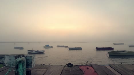 The-tranquil-rest-of-petite-fishing-vessels-atop-the-water,-embraced-by-mist-and-fog,-as-the-sun's-twilight-rays-bestow-a-calm-radiance,-elevating-the-essence-of-marine-life