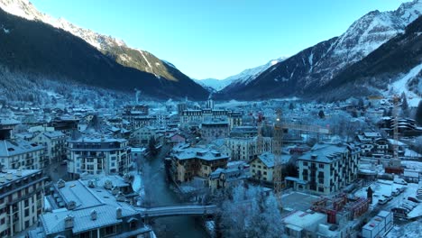 Low-drone-flyover-of-a-river-and-ski-village-of-Chamonix,-France-in-the-Alps-mountain-range-on-a-cold-winter-morning-with-snow-and-Ice