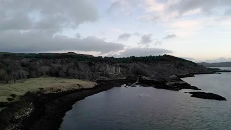 Dunvegan-castle-on-the-isle-of-skye,-surrounded-by-woodland-and-sea-at-dusk,-aerial-view