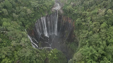 Aerial-tilts-down-to-huge-waterfall-grotto-on-Java,-Tumpak-Sewu