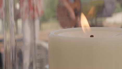 Close-up-of-a-burning-candle-in-a-lantern,-someone-playing-guitar-in-the-background