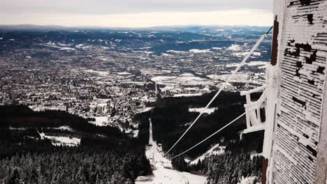 Frozen-chair-lift-cable-system-at-skiing-resort-mountainside,-city-in-background