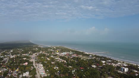 El-cuyo,-a-quaint-beach-town-on-the-yucatan-peninsula-with-lush-vegetation-and-a-long-pier-extending-into-the-sea,-daytime,-aerial-view