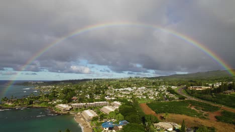 Perfect-vibrant-rainbow-over-tropical-coastline-and-hotels-with-grey-clouds,-Maui