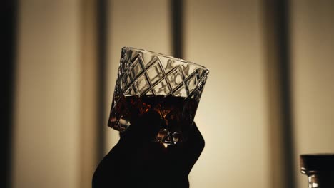 Eine-Hand-Schwenkt-Ein-Glas-Bourbon-Whisky-Im-Gegenlicht