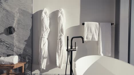 Schwenkaufnahme-Von-Weißen-Handtüchern-Und-Bademänteln,-Die-An-Der-Wand-Neben-Einer-Weißen-Freistehenden-Badewanne-In-Einem-Badezimmer-In-Einer-Hochhauswohnung-Hängen