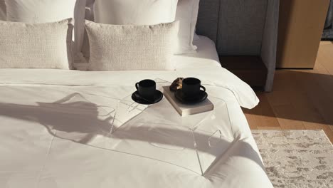 Nachttisch-Mit-Zwei-Schwarzen-Kaffeetassen-Und-Einem-Buch-Auf-Einem-Großen-Bett-Mit-Weißer-Bettwäsche