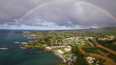 Beautiful-perfect-rainbow-arches-from-clear-ocean-to-green-vibrant-lush-mountains-above-homes-on-the-coast