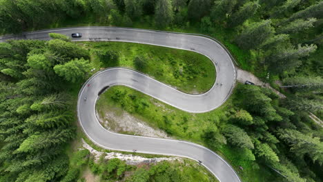 Cyclists-riding-curving-alpine-woodland-forest-road-aerial-top-down-view