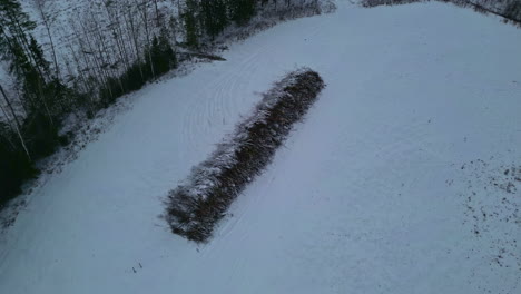 Circular-drone-view-over-a-pile-of-wood-stacked-in-a-snow-covered-meadow