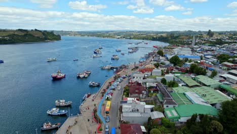 Aerial-view-circling-the-waterfront-of-Dalcahue,-in-partly-sunny-Chiloé,-Chile