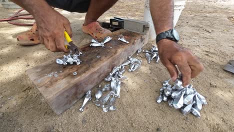 Person-using-pliers-to-handle-hot-molten-metal-poured-into-molds,-on-a-wooden-plank,-outdoors,-during-daytime