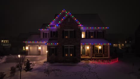 Large-American-home-covered-in-snow-and-multicolored-Christmas-lights-on-December-night