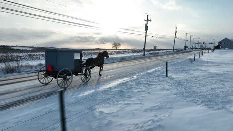 Amish-buggy-on-snowy-road-in-Lancaster-County,-PA,-under-a-sunset-sky