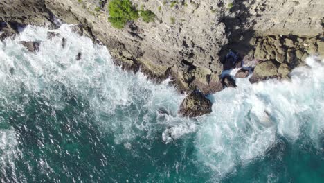 Aerial-top-down-forward-over-sea-waves-crashing-on-rocky-and-high-cliffs