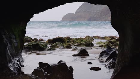 Erstaunliche-Nahaufnahme-Eines-Natürlichen-Felsbogenfensters-An-Der-Strandküste-Mit-Nebel,-Sand,-Moos,-Kieselsteinen-Und-Wellen,-Insel-Porto-Santo,-Madeira,-50fps-HD