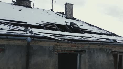 Eine-Drohne-Steigt-über-Ein-Beschädigtes-Und-Verlassenes-Gebäude-Mit-Teilweise-Eingestürztem,-Schneebedecktem-Dach-Auf