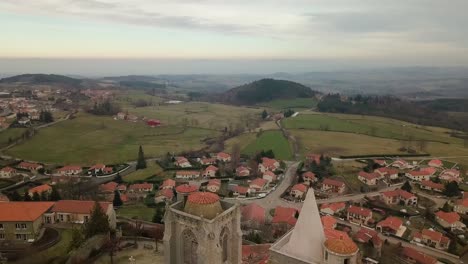 drone-shot-over-Saint-Bonnet-le-Chateau-collegiate-church-revealing-the-Monts-du-Forez-and-the-plaine-du-forez,-loire-departement-near-Saint-Etienne,-France