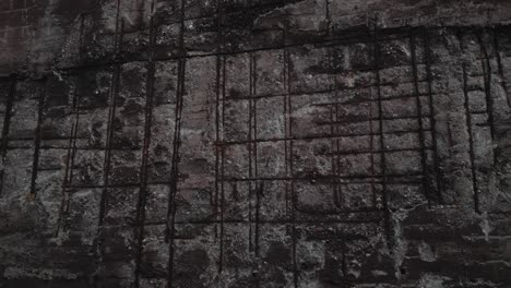 Close-up-of-a-weathered-concrete-wall-with-visible-rebar-grid-patterns,-exhibiting-signs-of-decay-and-corrosion