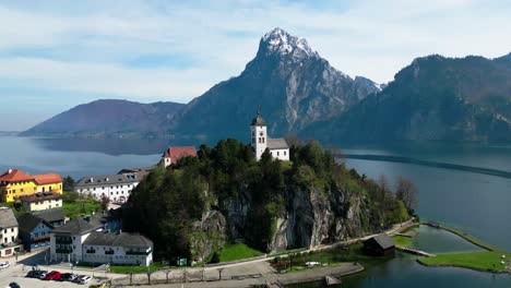 A-serene-church-perched-atop-a-cliff-in-austria-with-a-majestic-mountain-backdrop,-aerial-view