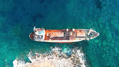 A-rusty-shipwreck-on-the-rocky-coast-of-cyprus,-clear-blue-waters,-top-down-aerial-view