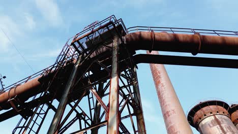 Rusted-industrial-structure-with-large-pipes-and-a-metal-framework-against-a-clear-blue-sky