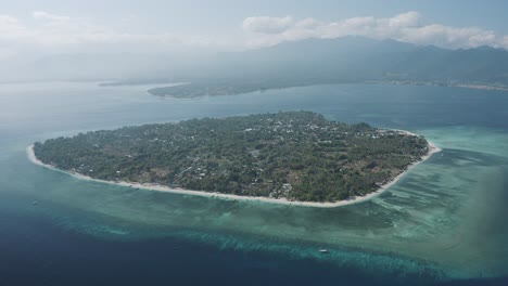 Aerial-shot-of-an-isolated-island-covered-with-trees-in-Thailand-with-seascape-and-range-of-mountains-at-background-during-daytime