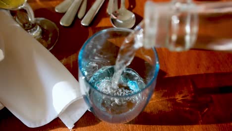 Zeitlupenaufnahmen-Von-Wasser-In-Glasflaschen,-Das-In-Ein-Glas-Auf-Einem-Gedeckten-Tisch-Gegossen-Wird