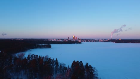 Drone-shot-over-snowy-ice-with-sunlit-Helsinki-Kalasatama-skyline-background