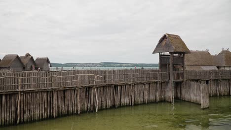 Thatched-roof-structures-on-stilts-over-water,-reminiscent-of-prehistoric-dwellings,-cloudy-day