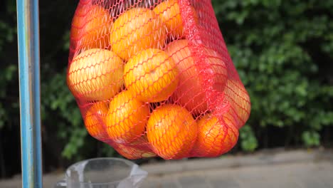 Frische-Orangefarbene-Früchte-In-Einem-Roten-Korb,-Orangen-Auf-Einem-Verschwommenen-Grünen-Hintergrund