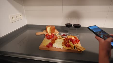 Woman-taking-pictures-of-a-cheeseboard-and-red-wine-with-a-phone